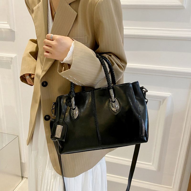 Person holding a black handbag against a white wall