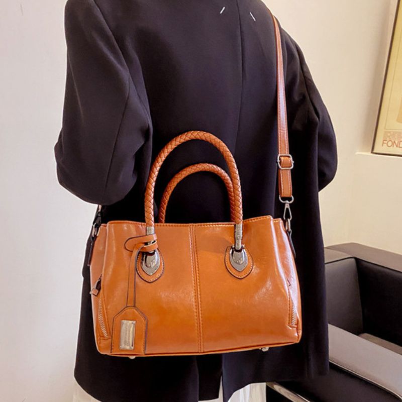 Person holding a brown leather handbag with a plain background