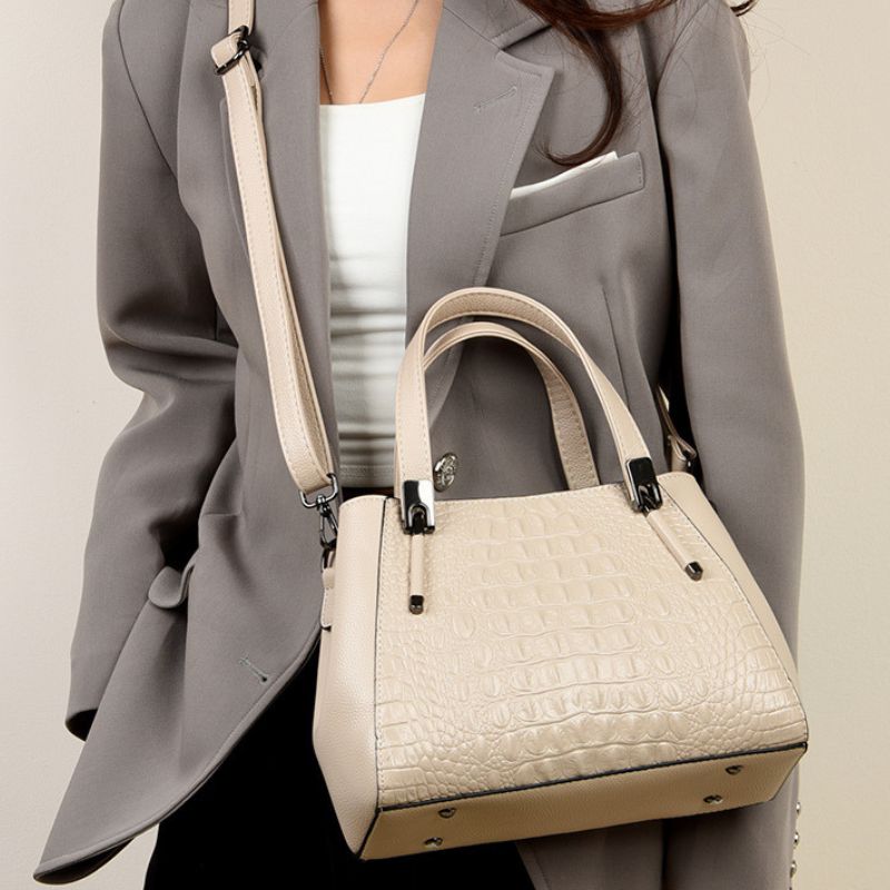 Person wearing a gray blazer with a beige handbag on a plain background
