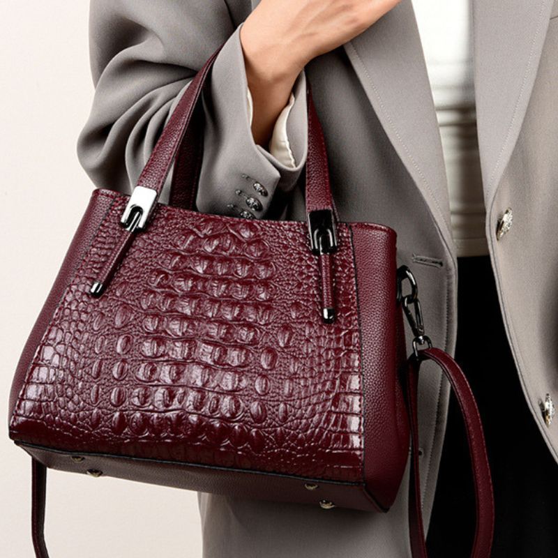 Maroon textured handbag held by a person wearing a gray coat.