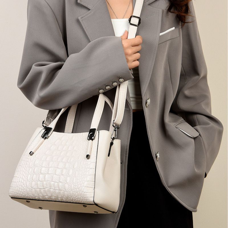 Person wearing a gray coat holding a white handbag against a neutral background