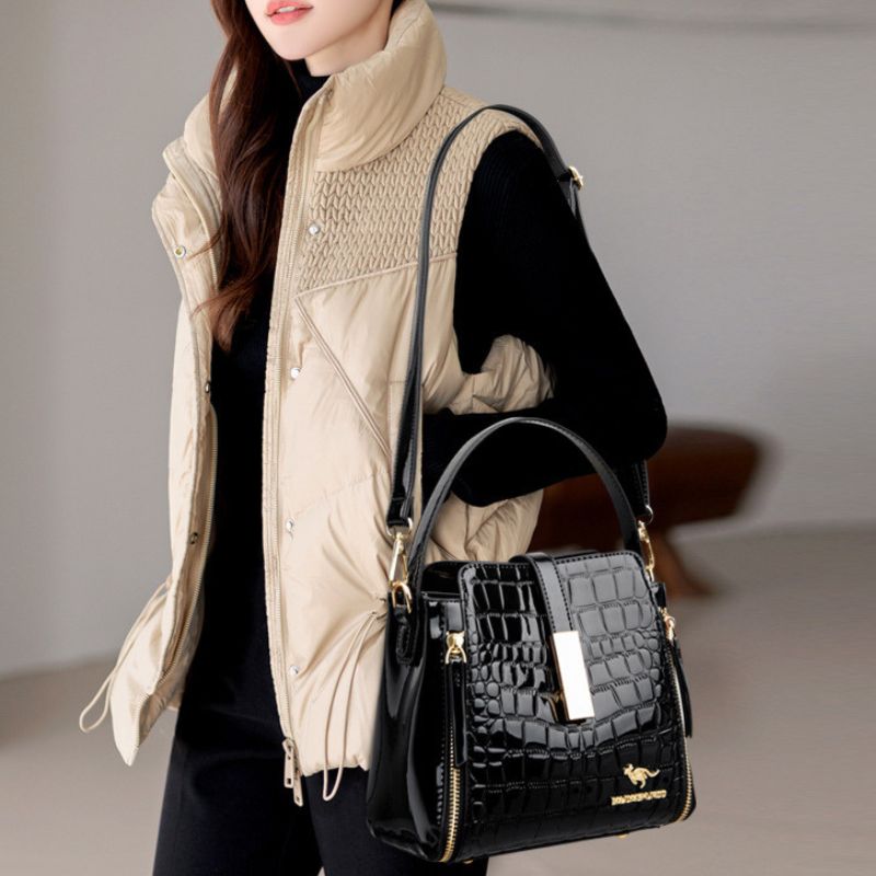 Person holding a black handbag with a visible brand logo against a neutral background