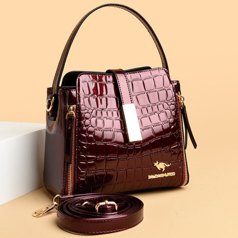 Brown handbag with crocodile texture and visible brand logo on a beige background