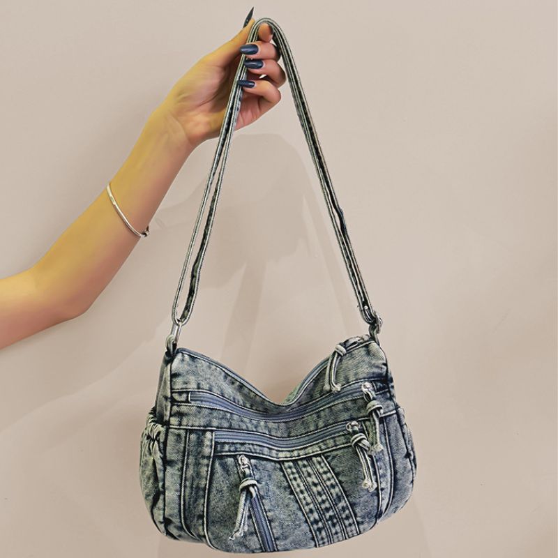 Denim handbag held by a hand against a beige background