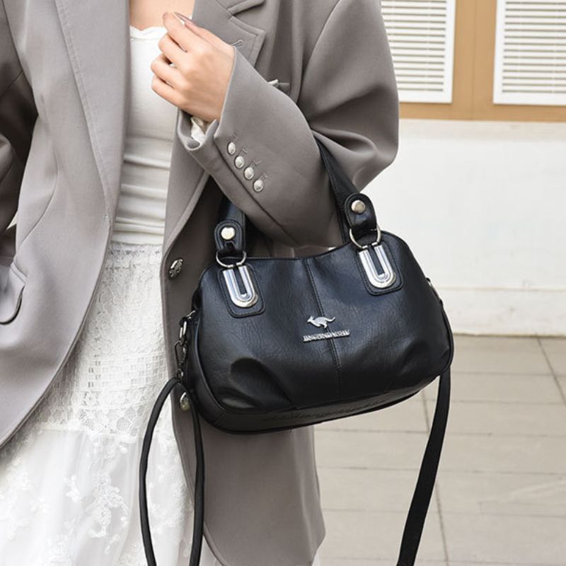 Person holding a black handbag with a visible brand logo indoors.