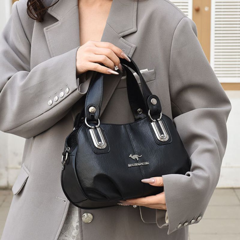 Person holding a black handbag with a visible brand logo, wearing a gray coat.
