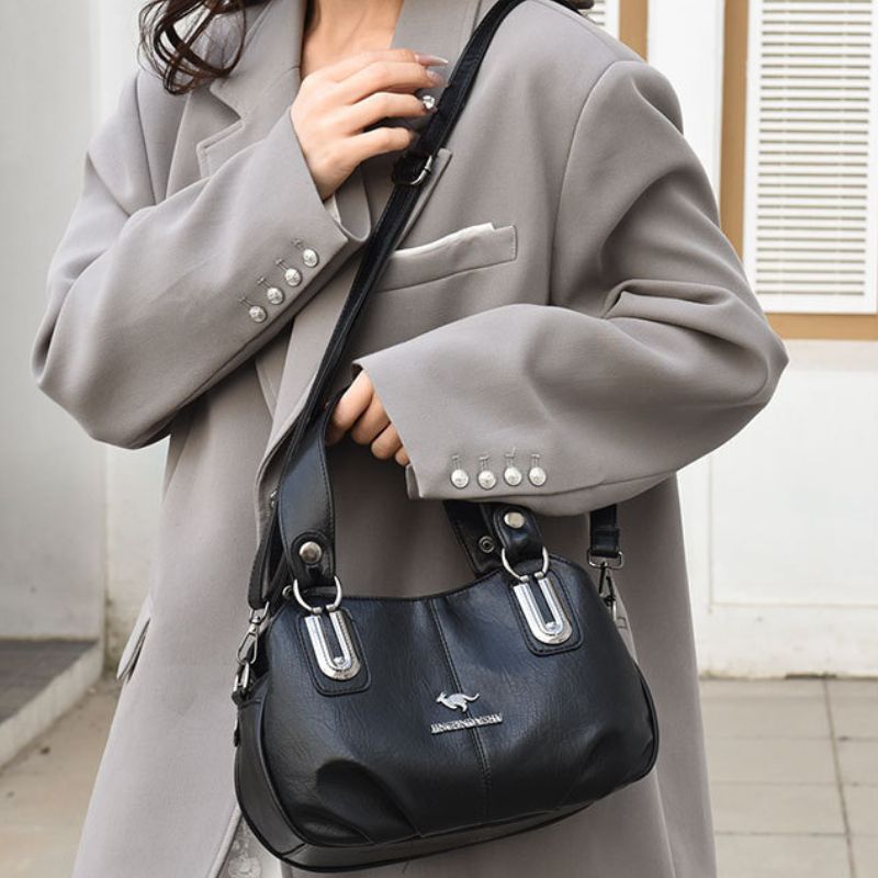 Person wearing a gray coat holding a navy handbag with a visible brand logo.