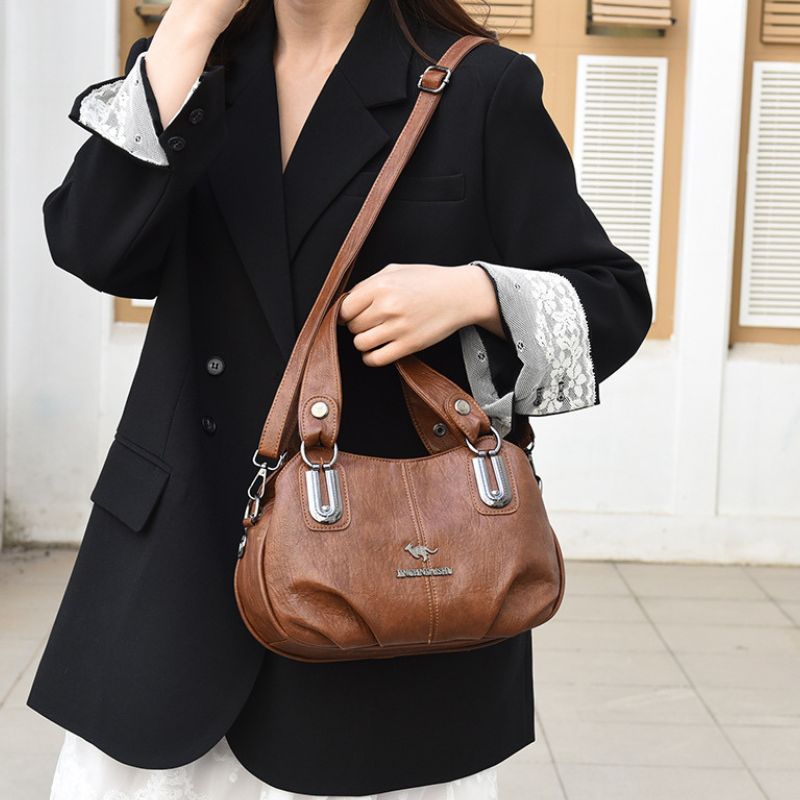 Person holding a brown leather handbag with a visible brand logo.