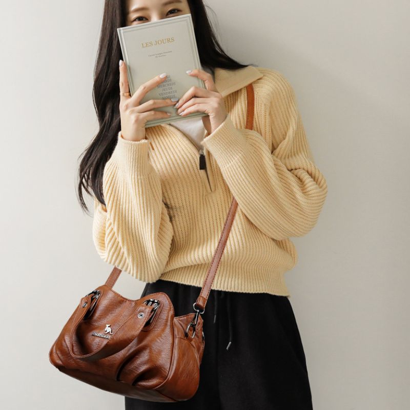 Woman holding a book and a brown leather bag against a plain background