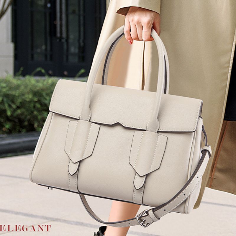 Beige handbag held by a person wearing a beige coat outdoors.