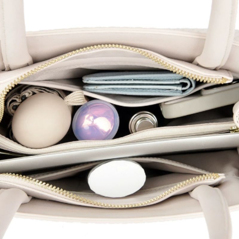 Open beige handbag with various items including a purple ball and a white egg.