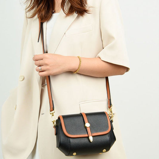 Person holding a black handbag with brown accents on a light background