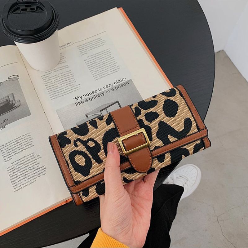 Leopard print wallet held by a hand with an open book and coffee cup in the background