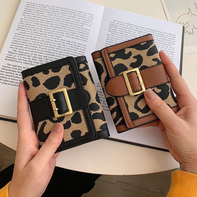 Two leopard print wallets with gold buckles held by hands on an open book.