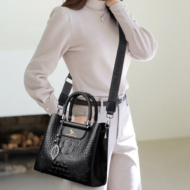 Person holding a black handbag with a visible brand logo against a neutral background