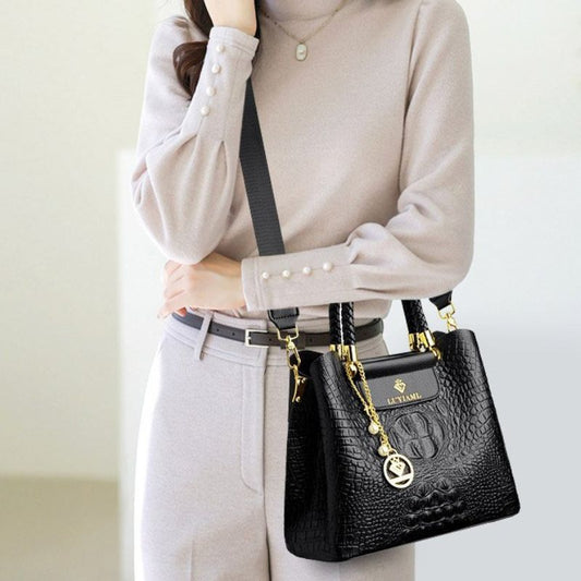 Person wearing a beige sweater and light gray pants with a black handbag featuring gold accents.