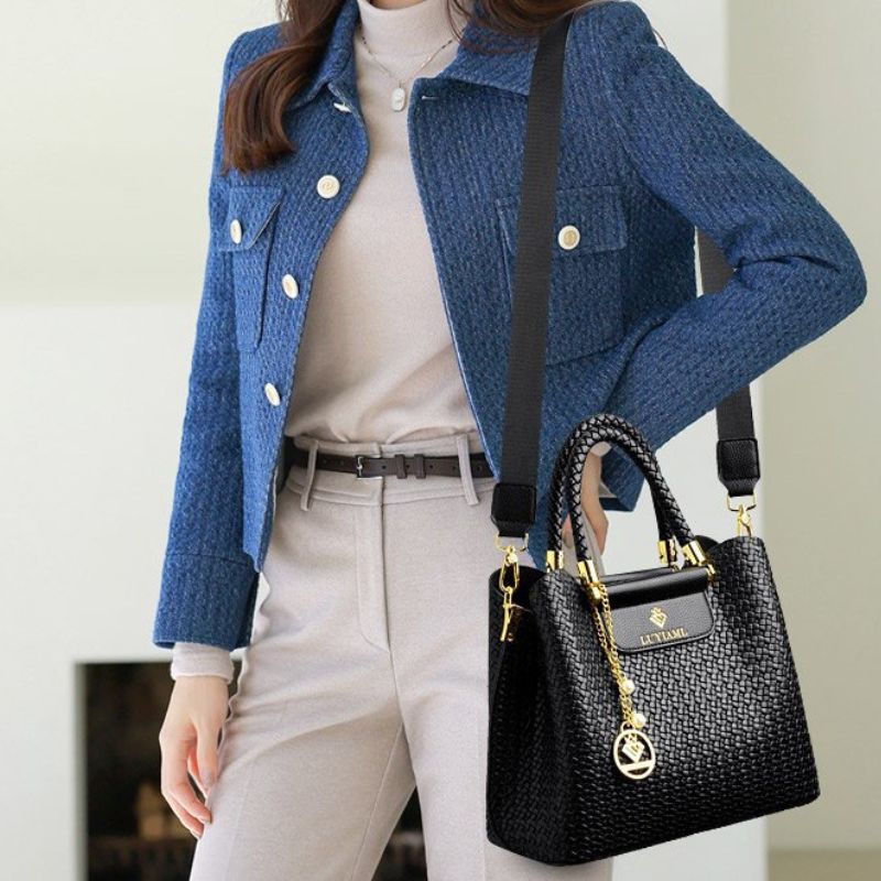 Person wearing a blue jacket holding a black handbag with gold accents.