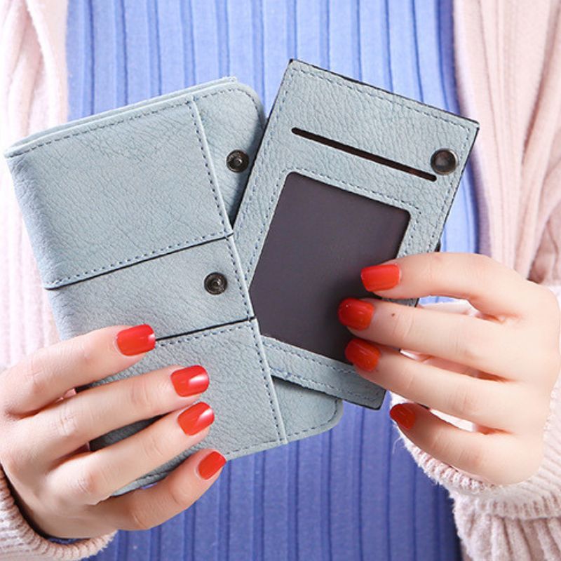 Light blue cardholder with multiple card slots held by hands with red nail polish against a blurred background.