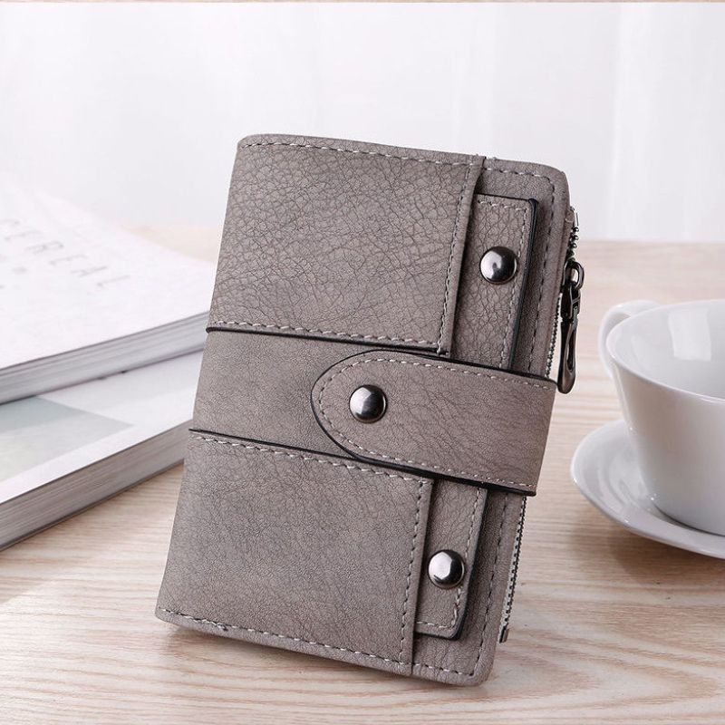 Gray wallet with metallic accents on a wooden surface with a cup and book in the background