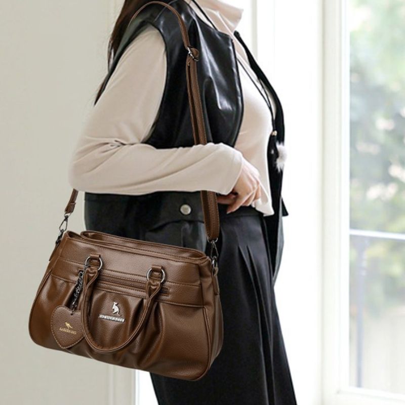 Person holding a brown handbag with a visible brand logo indoors.