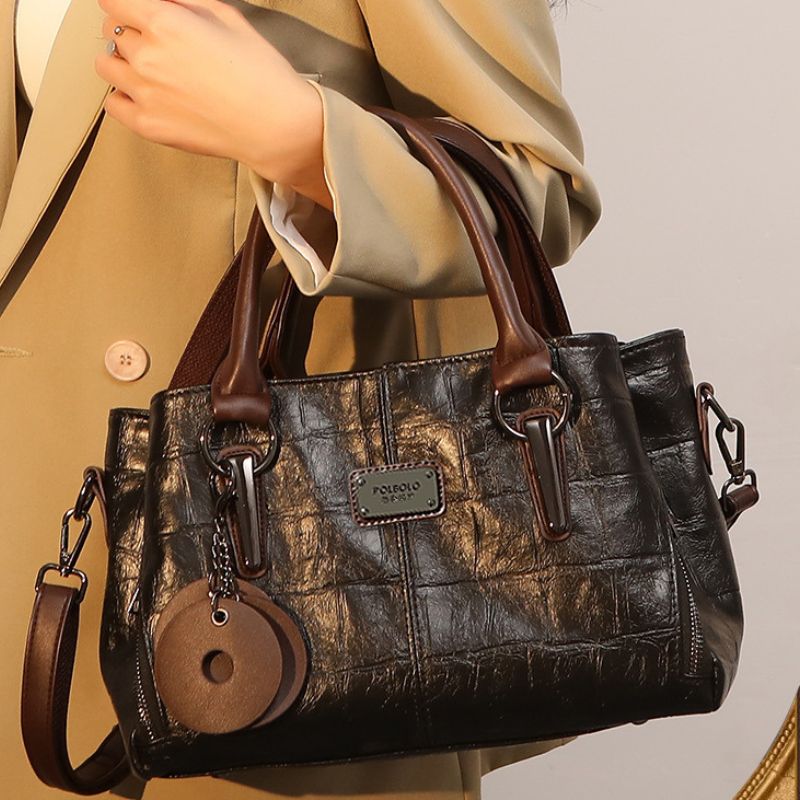 Brown textured handbag with leather accents held by a person wearing a beige coat.