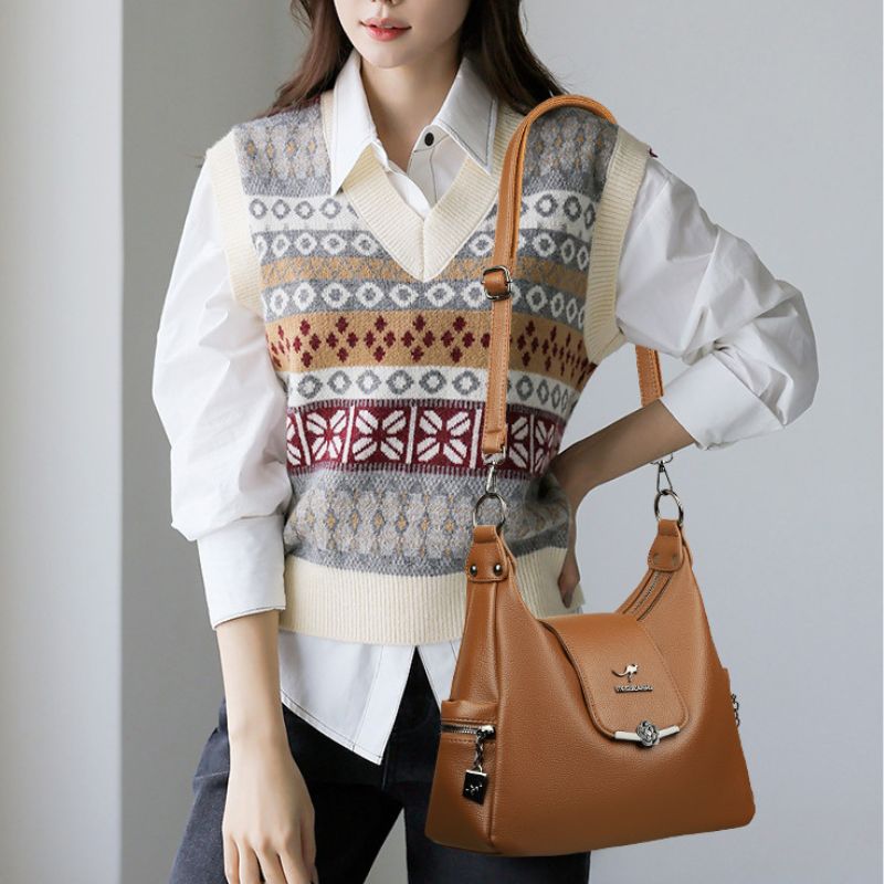 Person wearing a patterned vest and white shirt, holding a brown handbag against a plain background