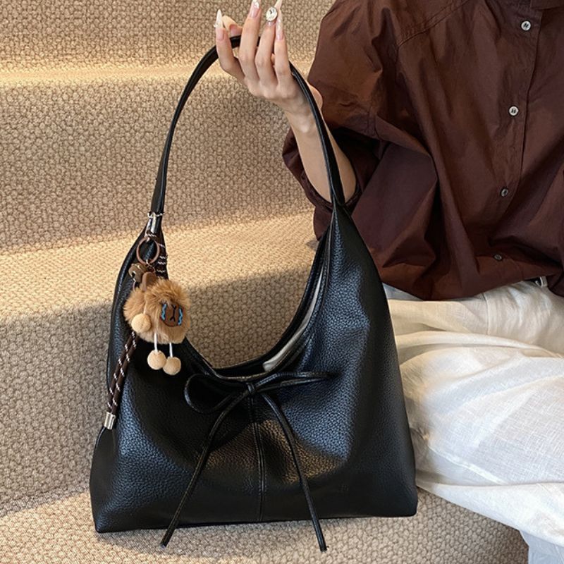 Black handbag with a decorative charm held by a person wearing a brown shirt.
