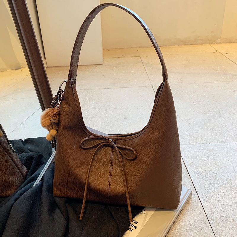 Brown color ladies hand bag placed above the book and jacket.