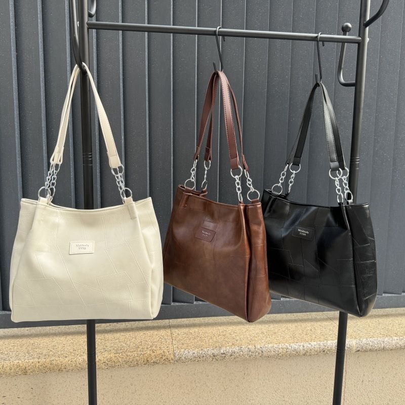 Three handbags in beige, brown, and black hanging on a rack against a gray wall.