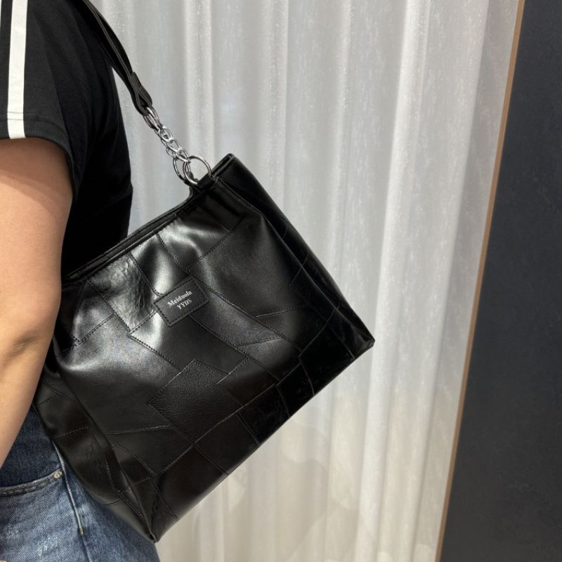 Person holding a black quilted handbag with a chain strap against a neutral background