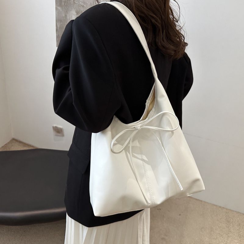 woman have white color soft leather hand bag or tote bag on her shoulder, wearing black color coat.