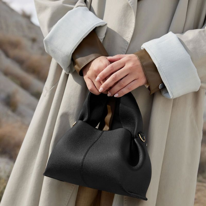 Person holding a black handbag with a neutral-toned coat in a natural setting