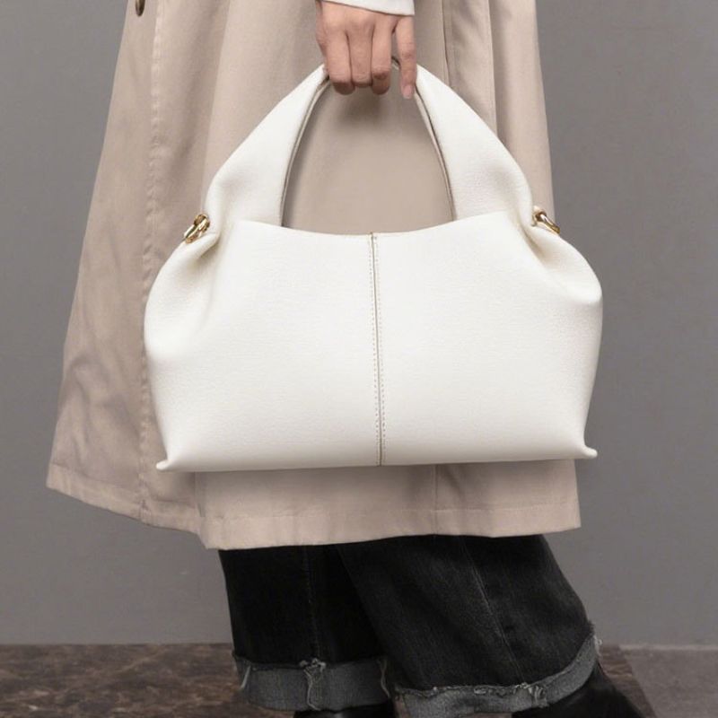White handbag held by a person wearing a beige coat against a gray background