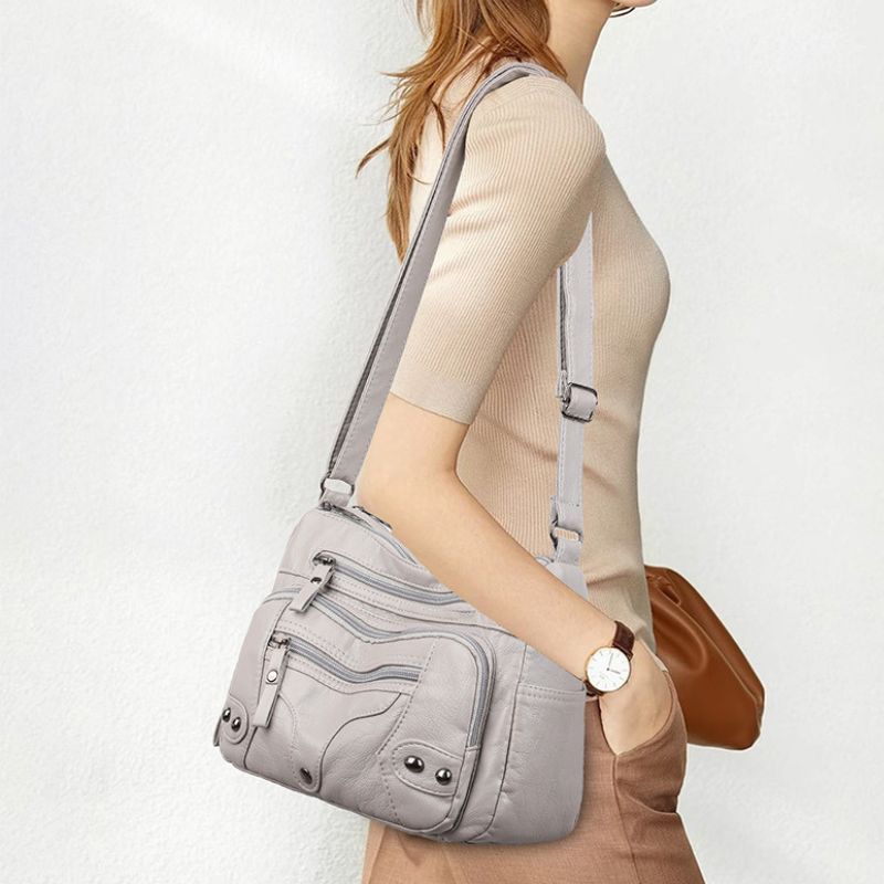 Person wearing a gray crossbody bag with a plain background