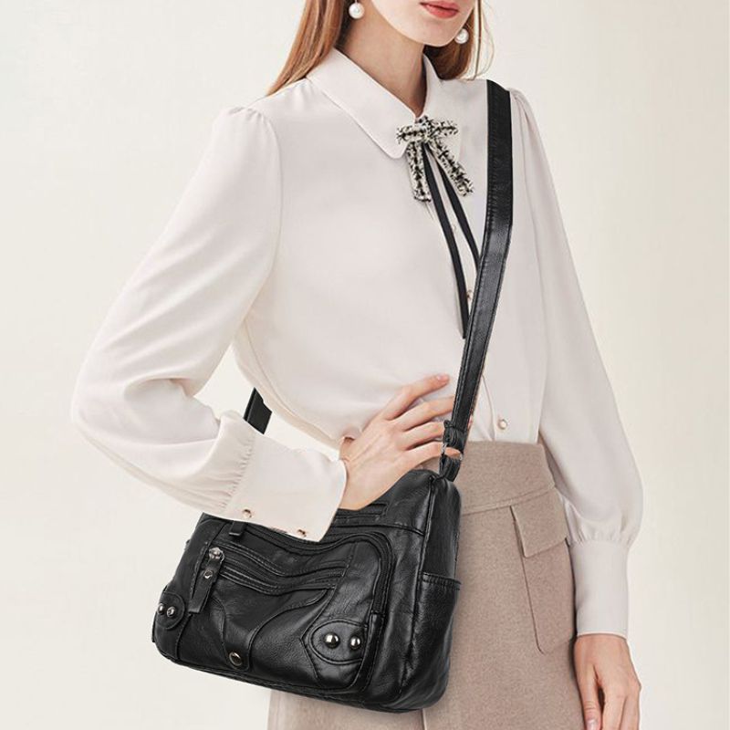 Person wearing a white blouse with a black leather handbag on a plain background