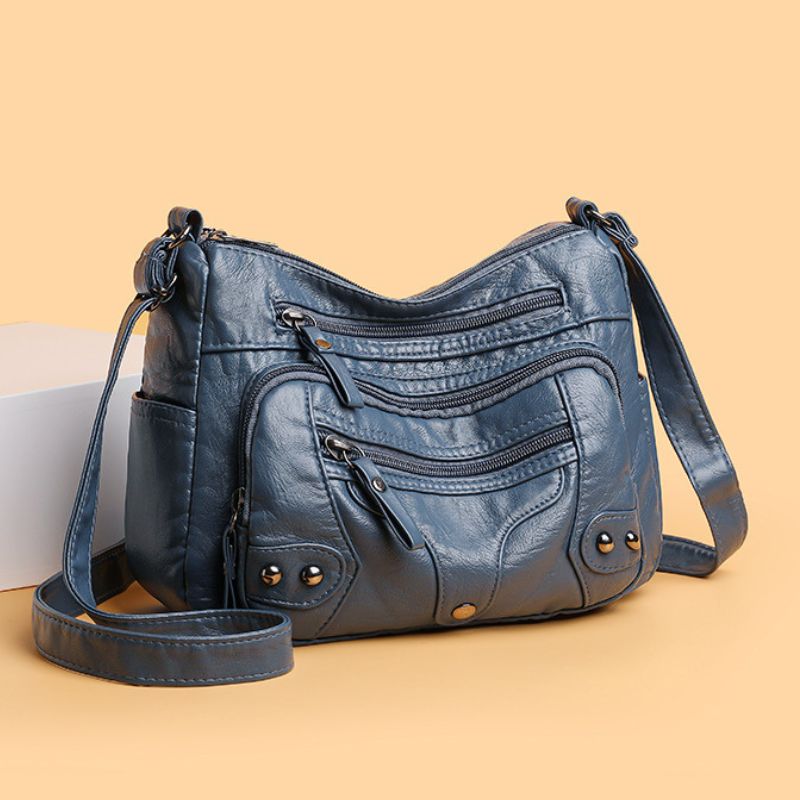 Blue leather handbag with multiple zippers on a beige background