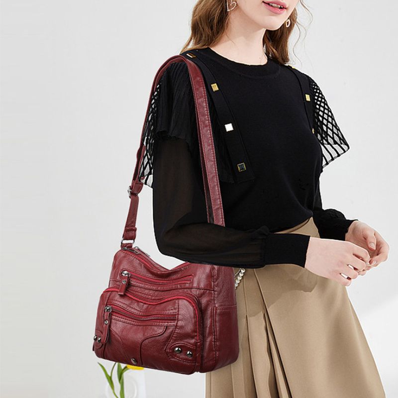 Person wearing a black top with sheer sleeves and beige pants, carrying a red handbag on a white background