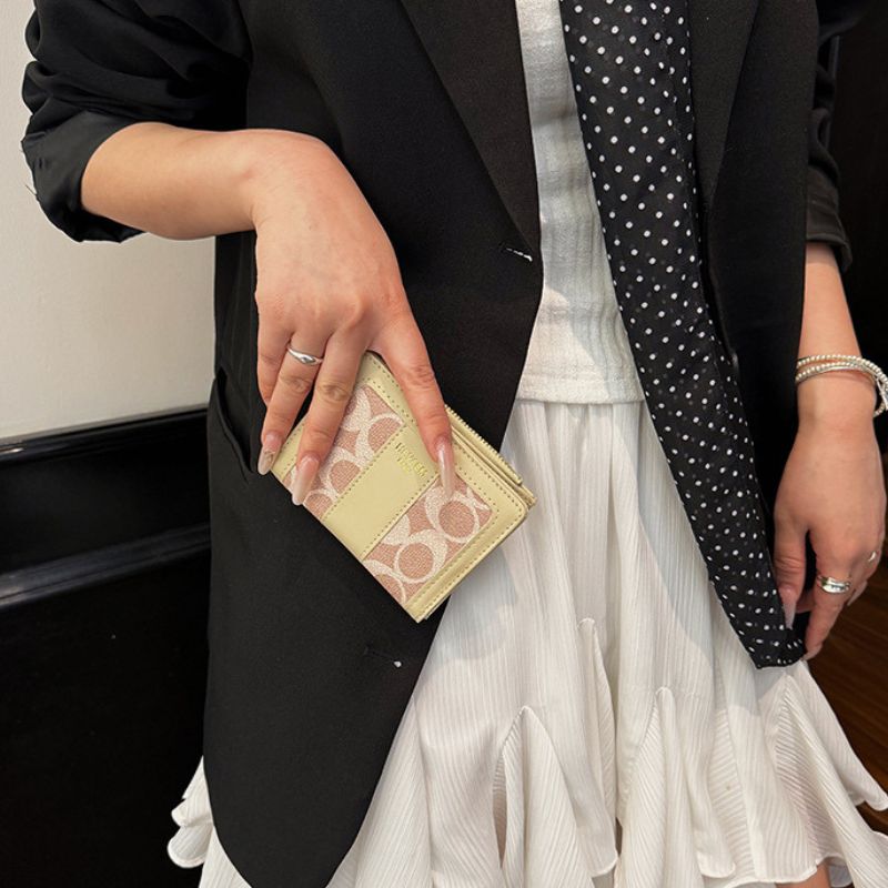 Person holding a beige wallet with a brand logo, wearing a black blazer and white skirt.