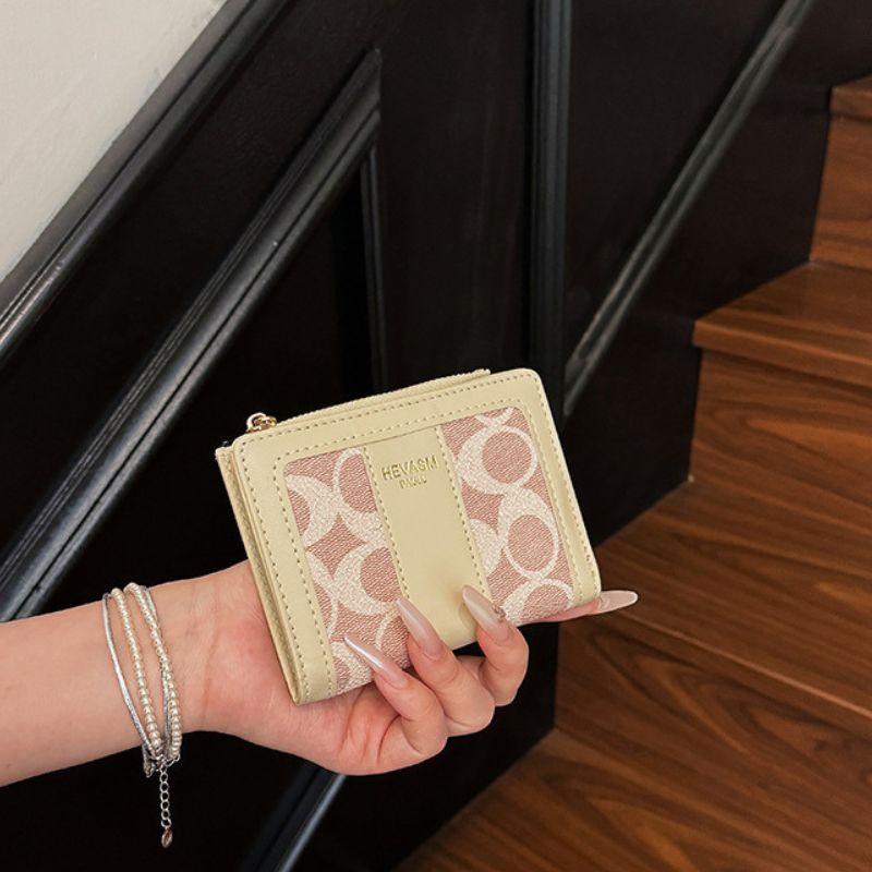 Hand holding a light-colored wallet with lace design, blurred background