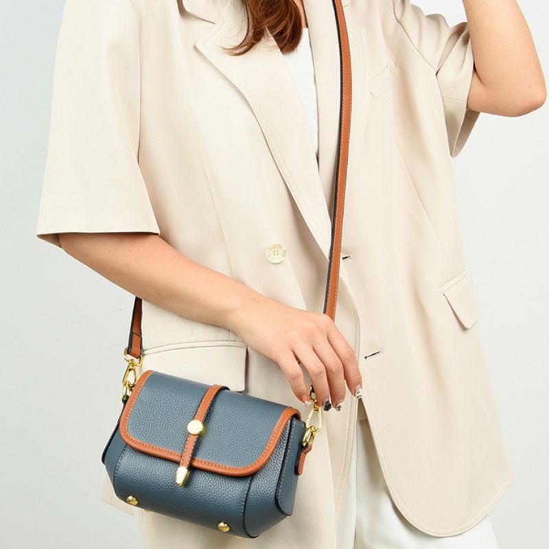 Person holding a blue handbag with brown accents against a light background