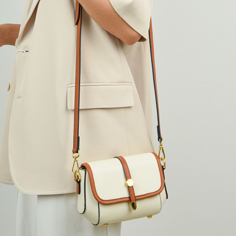 Beige handbag with brown accents worn by a person in a beige outfit on a light gray background