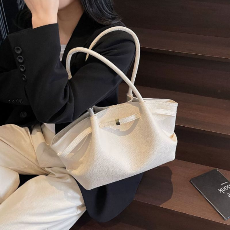 white color ladies handbag purse hanging on women shoulder wearing black coat sitting on stairs.
