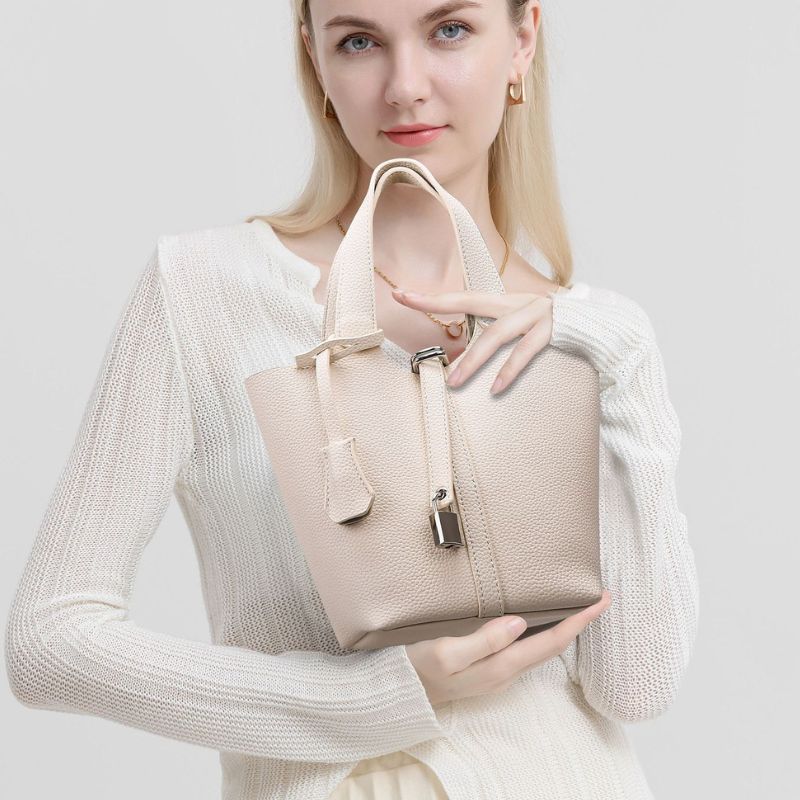 Woman holding a beige handbag against a plain background