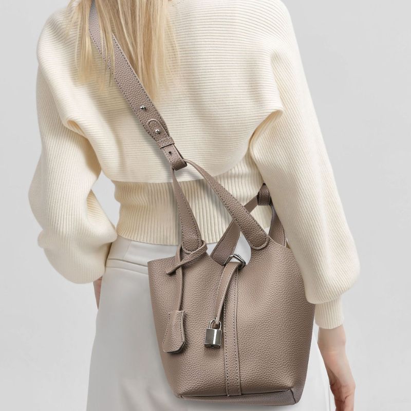 Person wearing a beige sweater and holding a matching beige handbag on a light gray background