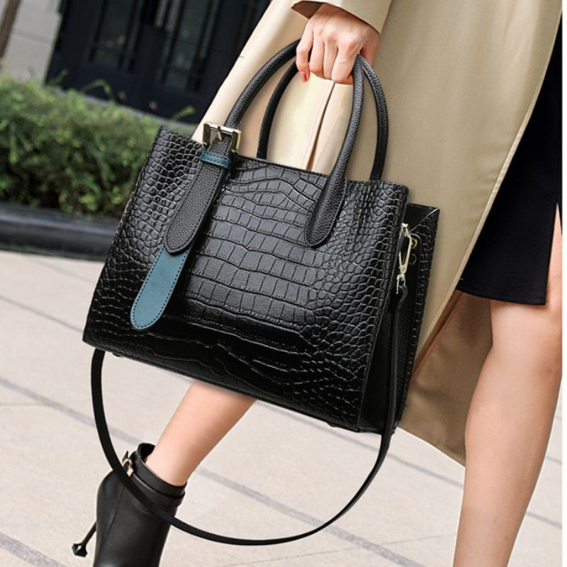 Person holding a black textured handbag with a blue strap outdoors.
