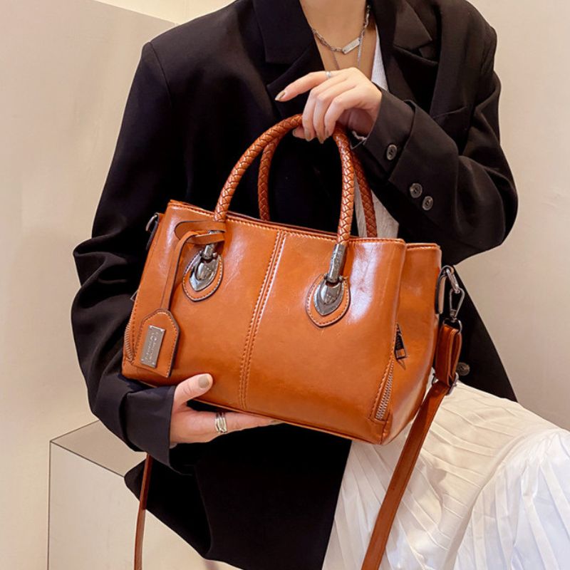 Person holding a brown leather handbag with a neutral background