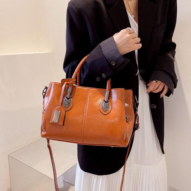 Person holding a brown leather handbag against a neutral background