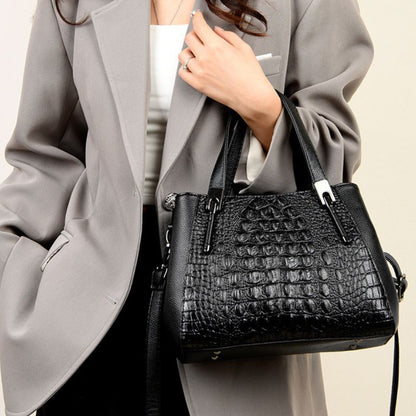 Person holding a black crocodile-patterned handbag against a neutral background