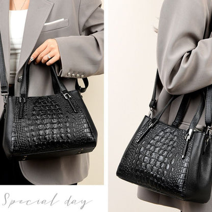 Black crocodile-patterned handbag held by a person wearing a gray suit.