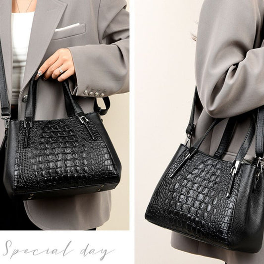 Black crocodile-patterned handbag held by a person wearing a gray suit.